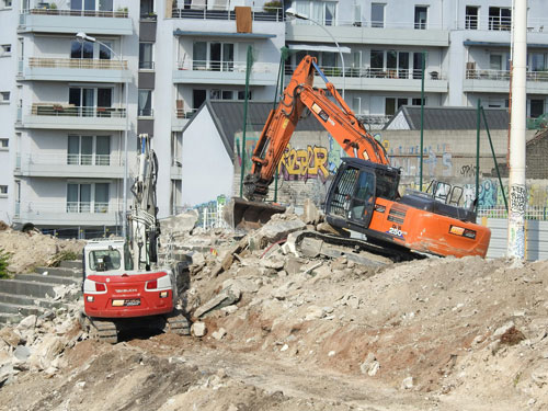 a construction site with a large orange excavator and a small red truck